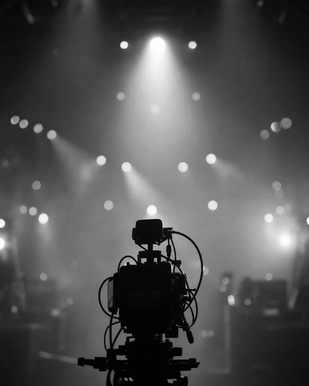 Core Media Co. brand imagery: the silhouette of a camera on a tripod facing a bank of stage lights through haze.